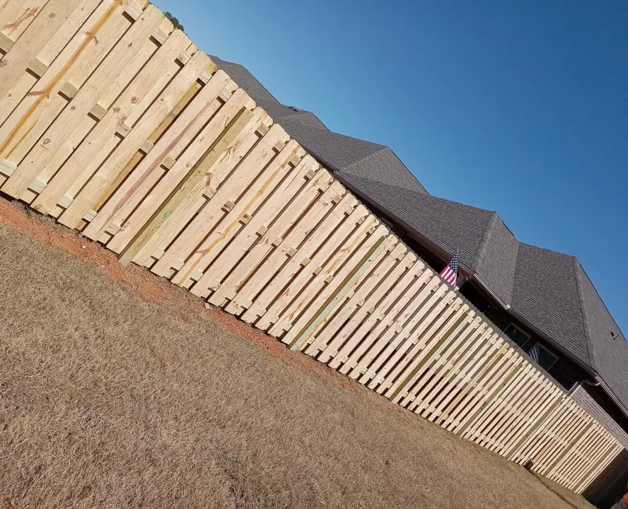 Natural wood picket fence following sloped ground beside a home flying an American flag
