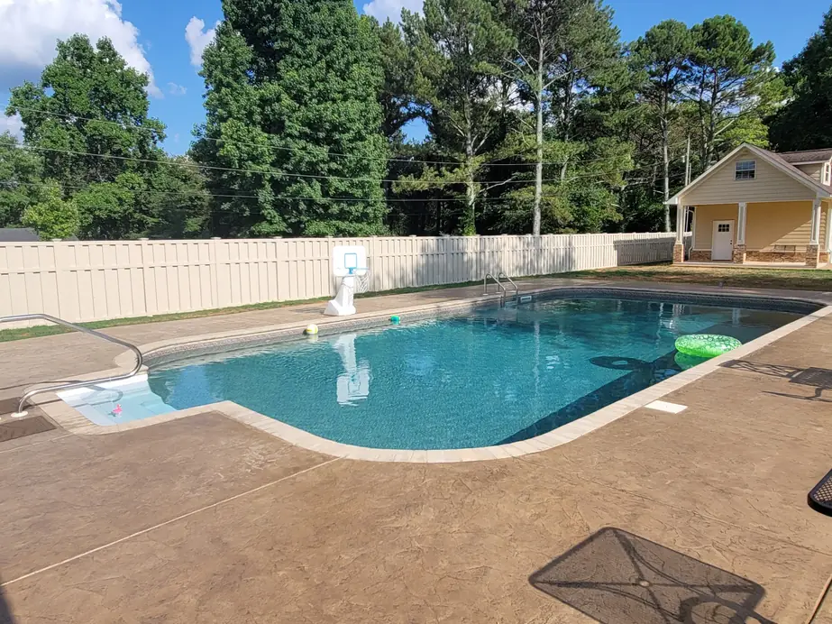 Cream vinyl privacy fence enclosing an in ground pool and pool house