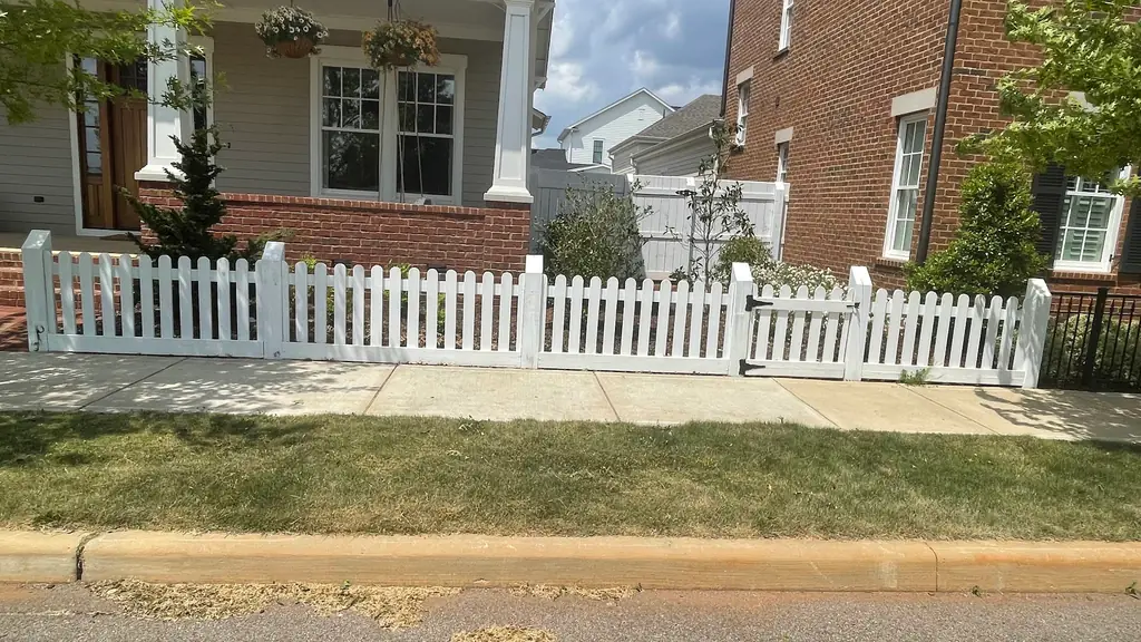 White painted picket fence and gate across the front yard of a brick craftsman home